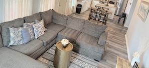 A modern living room with a sectional sofa, a coffee table, and a kitchen in the background. - 50 yards to sand and views, the best value for proximity! (Bolivar Peninsula)