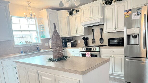 A modern kitchen with white cabinetry, stainless steel appliances, and a central island with a decorative vase. - 50 yards to sand and views, the best value for proximity! (Bolivar Peninsula)