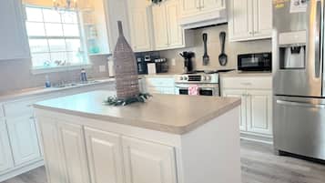 A modern kitchen with white cabinetry, stainless steel appliances, and a central island with a decorative vase.