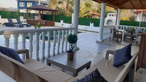 Een overdekt terras met een zwembad, ligstoelen en een pergola.
