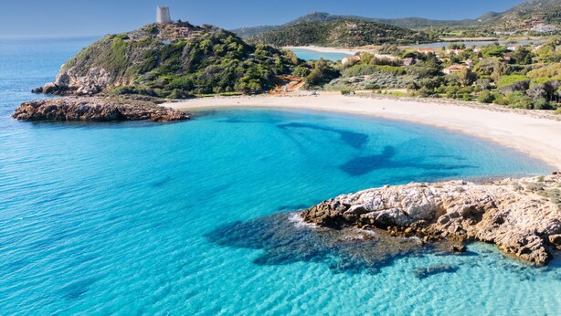 Un paysage côtier caractérisé par des eaux turquoise limpides, des rivages rocheux et un château perché sur une colline.