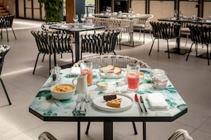 Un comedor con mesas preparadas para el desayuno, incluyendo platos de comida, cubiertos y bebidas.
