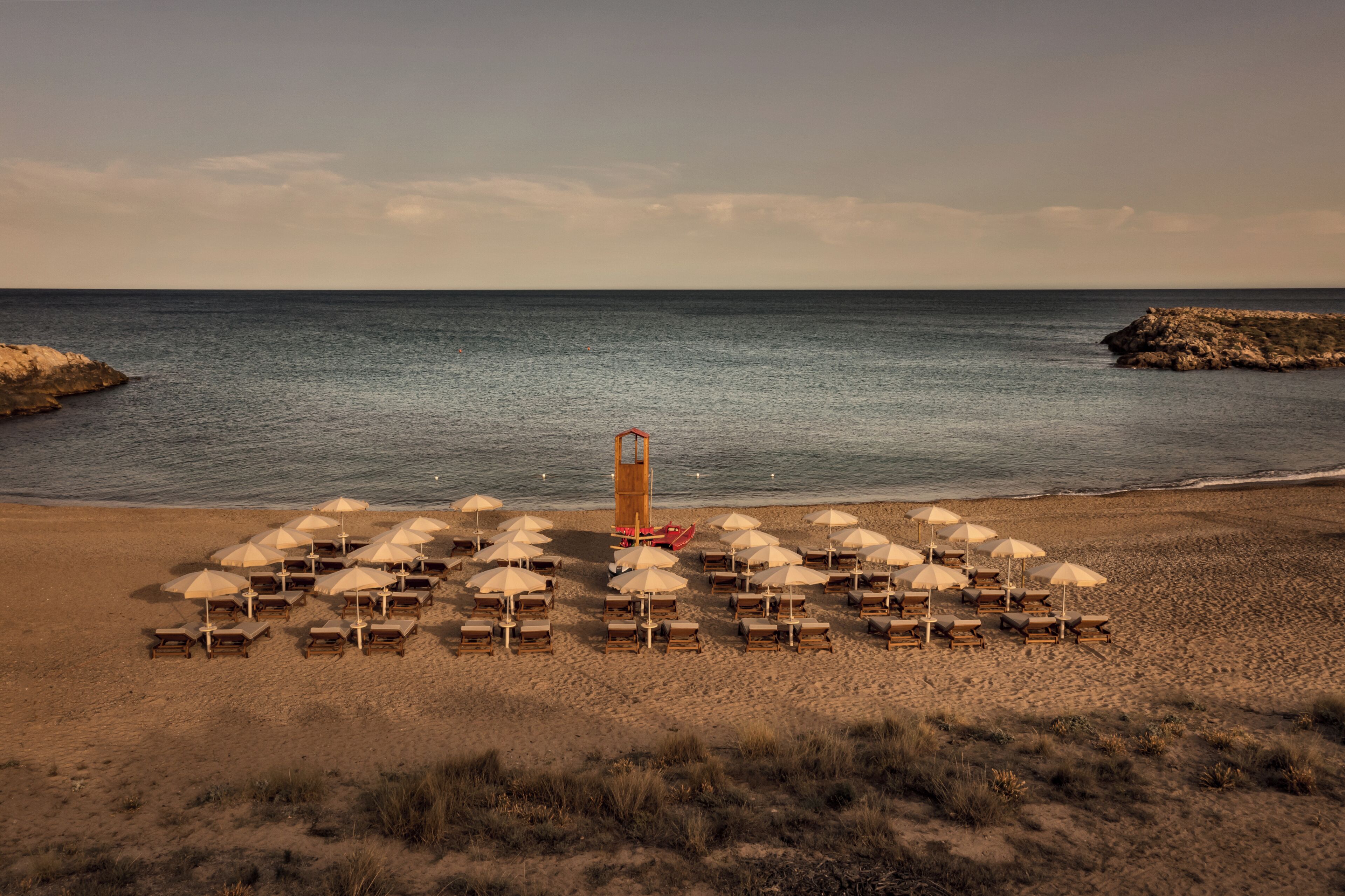 A beach with rows of sun loungers and umbrellas, a lifeguard tower, and the ocean in the background.