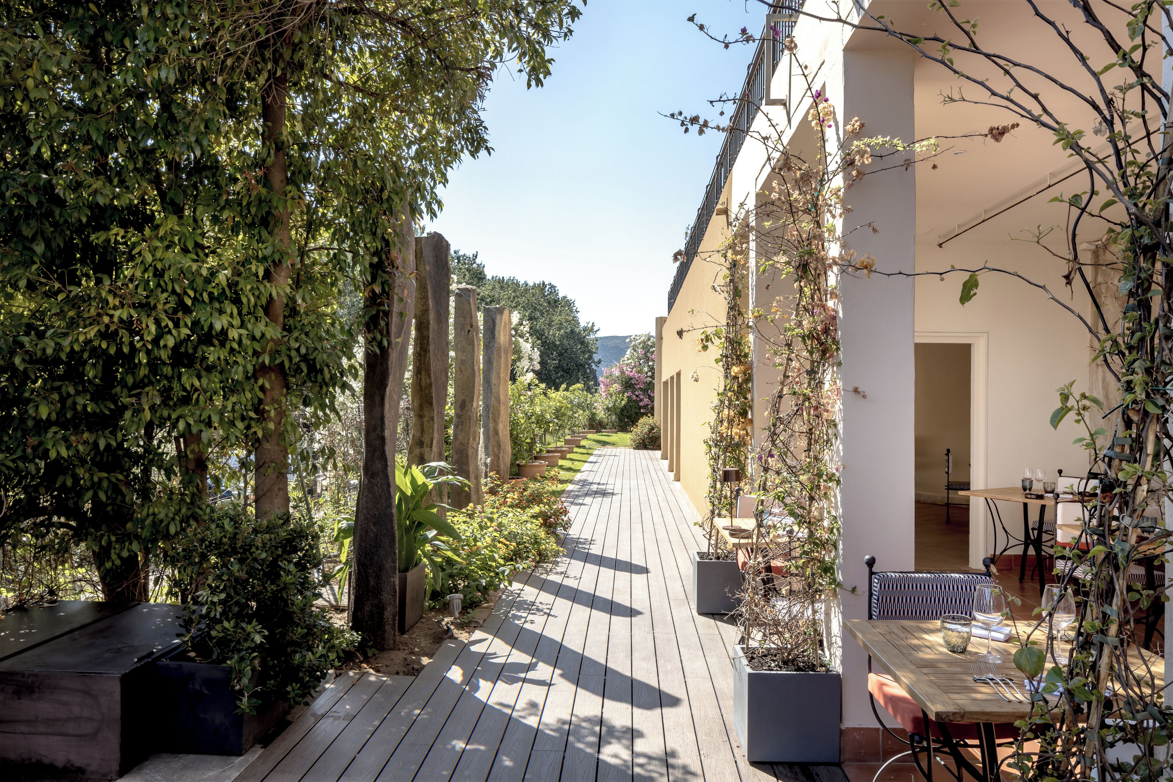 Una terraza de madera con macetas, una mesa con sillas y un edificio con balcón.