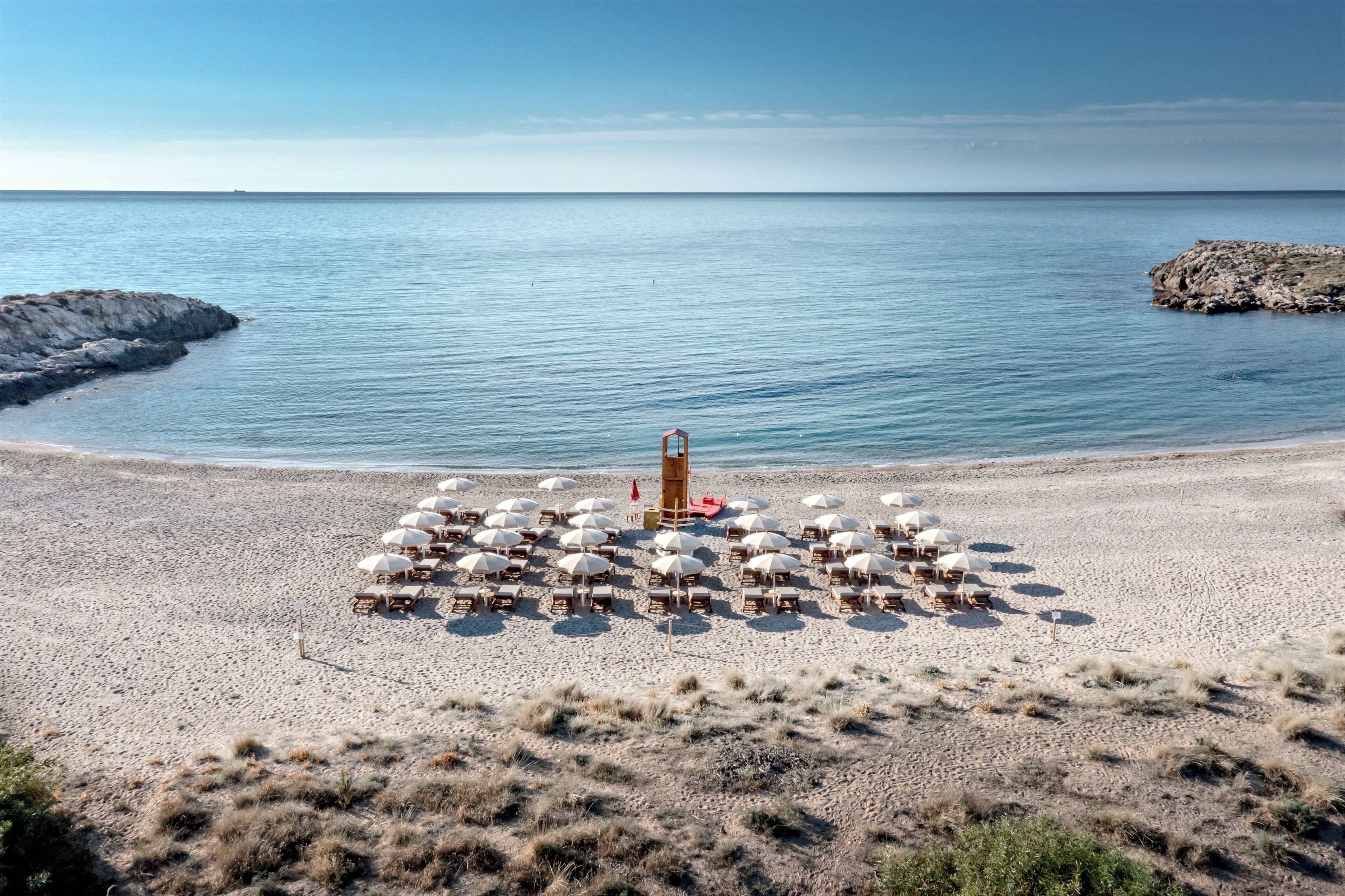 Una playa con numerosos sombrillas y sillas de playa dispuestas en círculo, centradas en torno a una pequeña estructura.