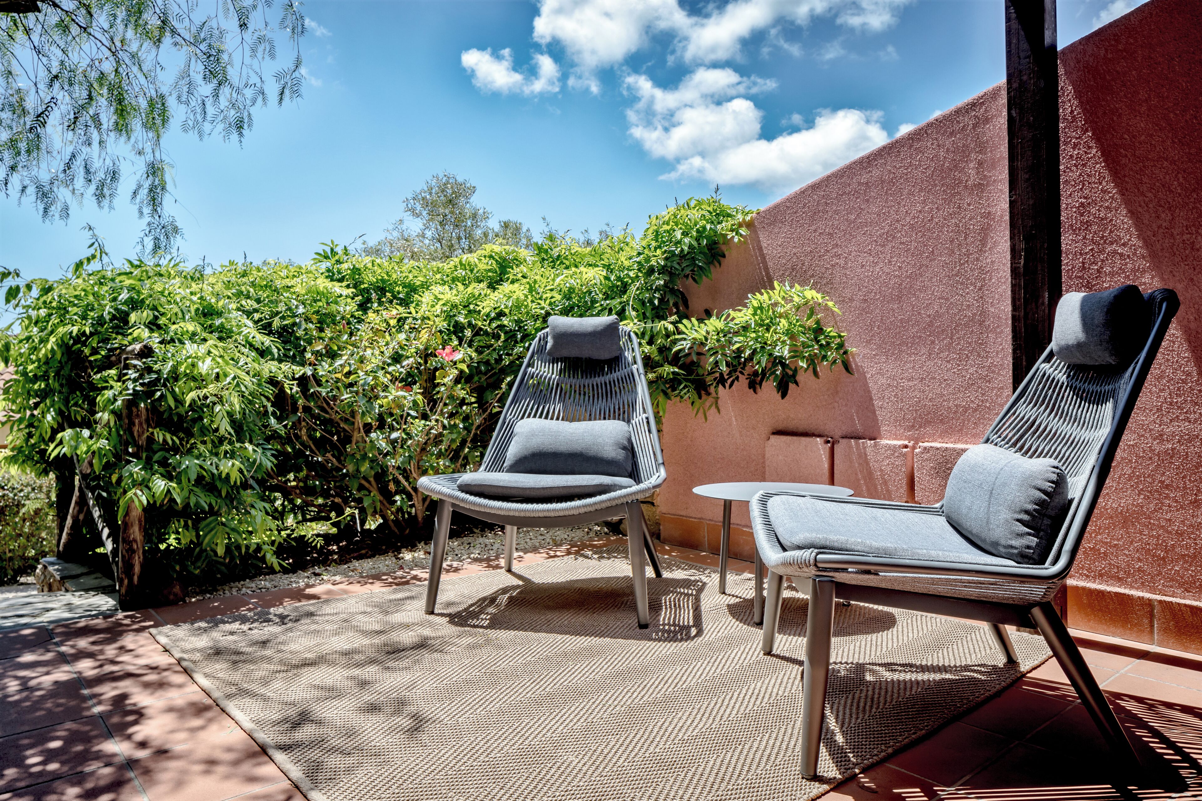 A patio with two wicker lounge chairs, a small round table, and a potted plant.
