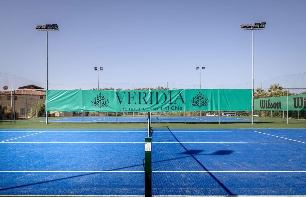 A tennis court with a banner reading 'VERIDIA the nature resort of Chia' and 'Wilson' brand tennis balls.