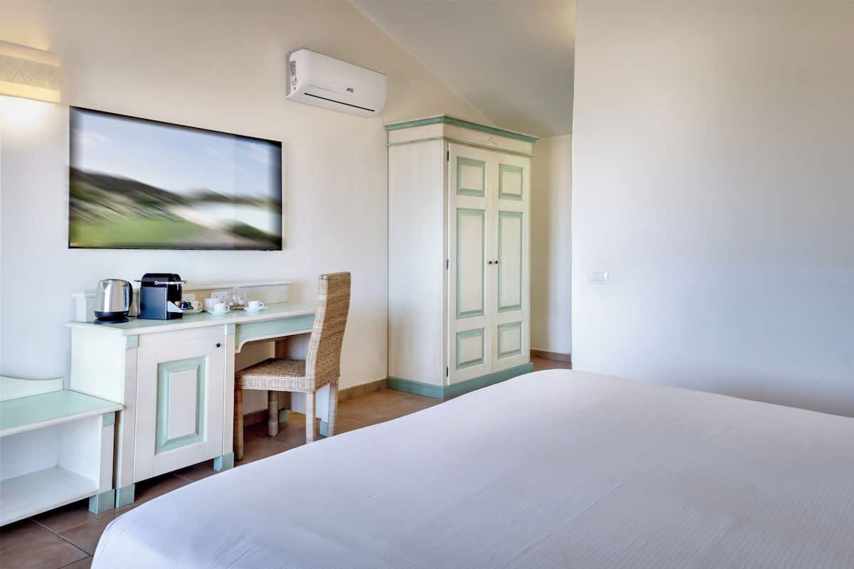 A hotel room with a bed, a desk with a chair, a TV, and a wardrobe.