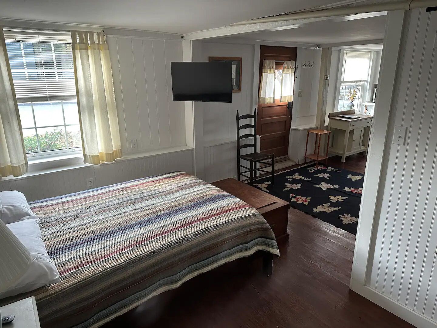 A room with a bed, a television, a chair, a desk, and a window with curtains.