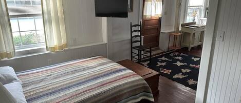 A room with a bed, a television, a chair, a desk, and a window with curtains.