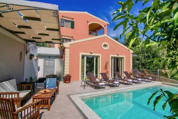 A two-story building with a swimming pool, outdoor seating, and a covered patio area.