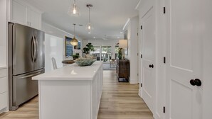 A modern kitchen with white cabinetry, a stainless steel refrigerator, pendant lighting, and a large island with a bowl.