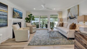 A spacious living room with a white sofa, beige armchairs, a coffee table, and a large window offering a view of the outdoors.