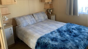 Une chambre à coucher comprenant un lit, deux tables de chevet, une lampe, une petite armoire et une fenêtre avec des rideaux.