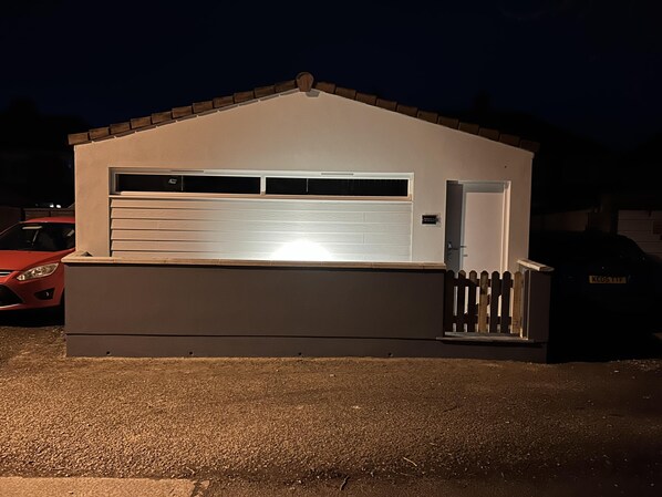 A small, single-story building with a garage door, a small porch, and a wooden fence.