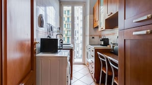 Une cuisine étroite avec des meubles de rangement en bois, un réfrigérateur blanc et une fenêtre donnant sur un balcon.