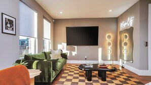 A modern living room with a green sofa, a checkered rug, and a flat-screen TV mounted on the wall. - ROOFTOP HOT TUB- FIRE PIT- MASSIVE CITY VIEWS (Nashville)