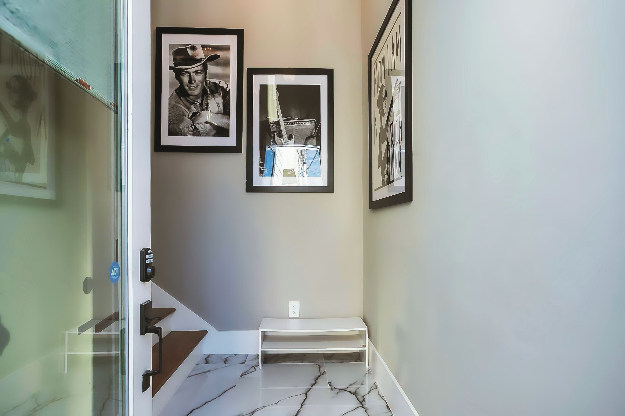 A hallway with a marble floor, a staircase with a white handrail, and three framed pictures on the wall.