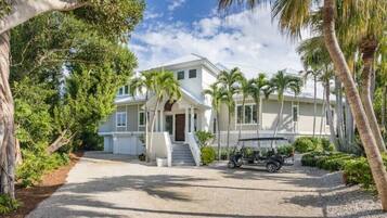 Stroll through lush gardens surrounded by palm trees and shrubs, leading to a modern two-story residence with a central entrance and golf cart access.