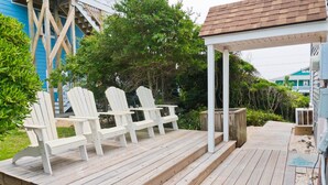 Une terrasse en bois avec des chaises Adirondack blanches et un espace salon abrité.