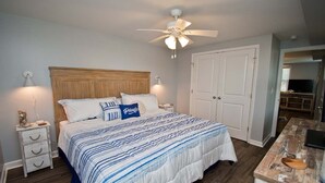 Une chambre à coucher comprenant un lit, des tables de chevet, un ventilateur de plafond et un bureau en bois.
