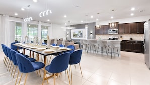 A modern kitchen with dark cabinets, a stainless steel refrigerator, and a large island with bar stools. - Windsor Island Resort 10br Villa Pool Near Disney 3063 (Davenport)