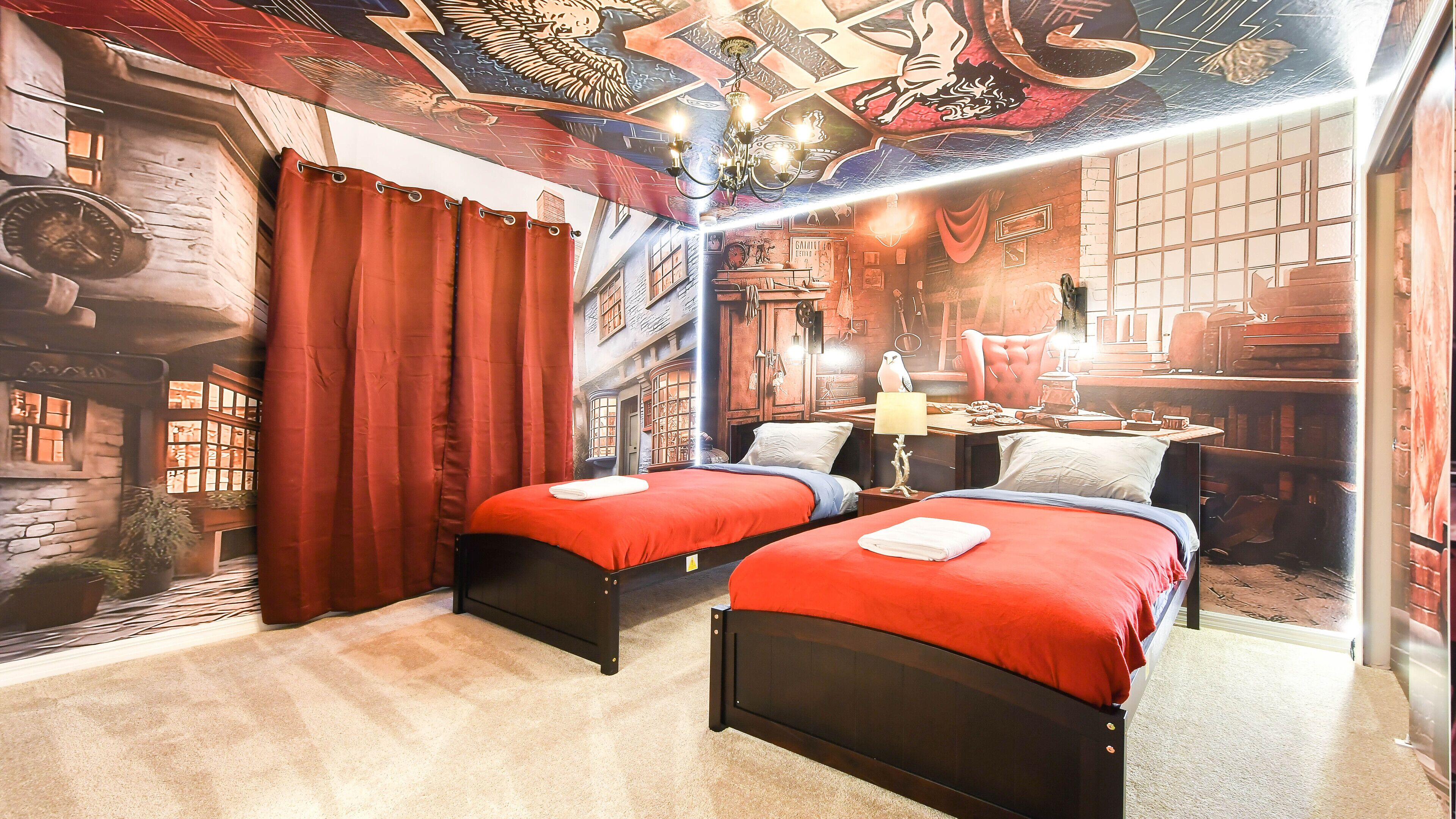 A room with two beds, red curtains, a chandelier, and a mural of a building.