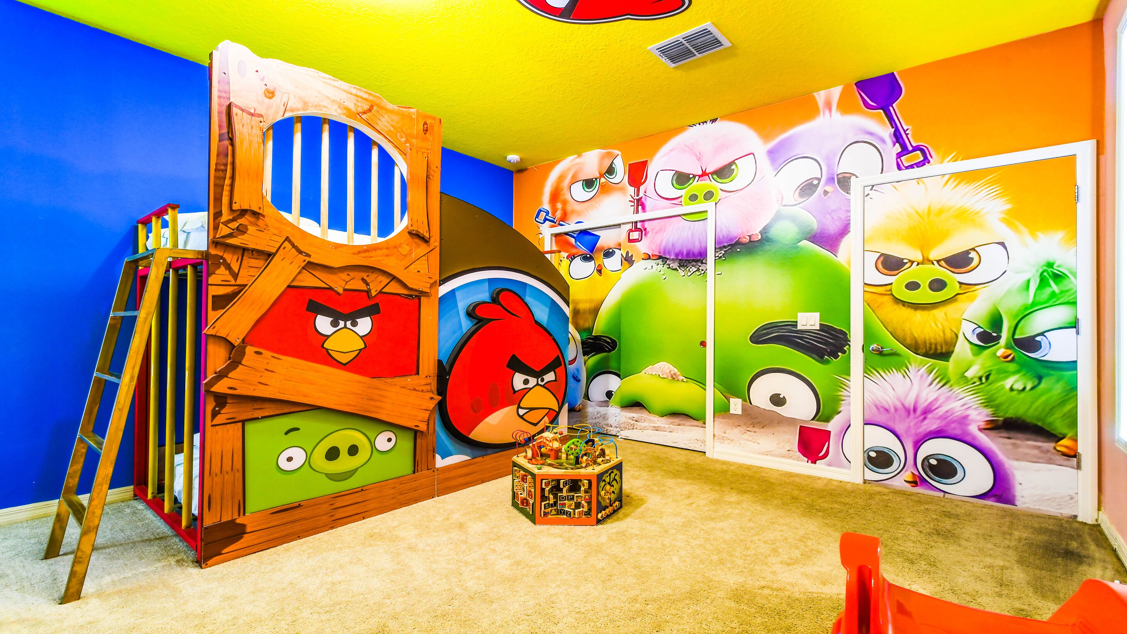 A room with a colorful mural of Angry Birds characters, a wooden playhouse, and a ladder.