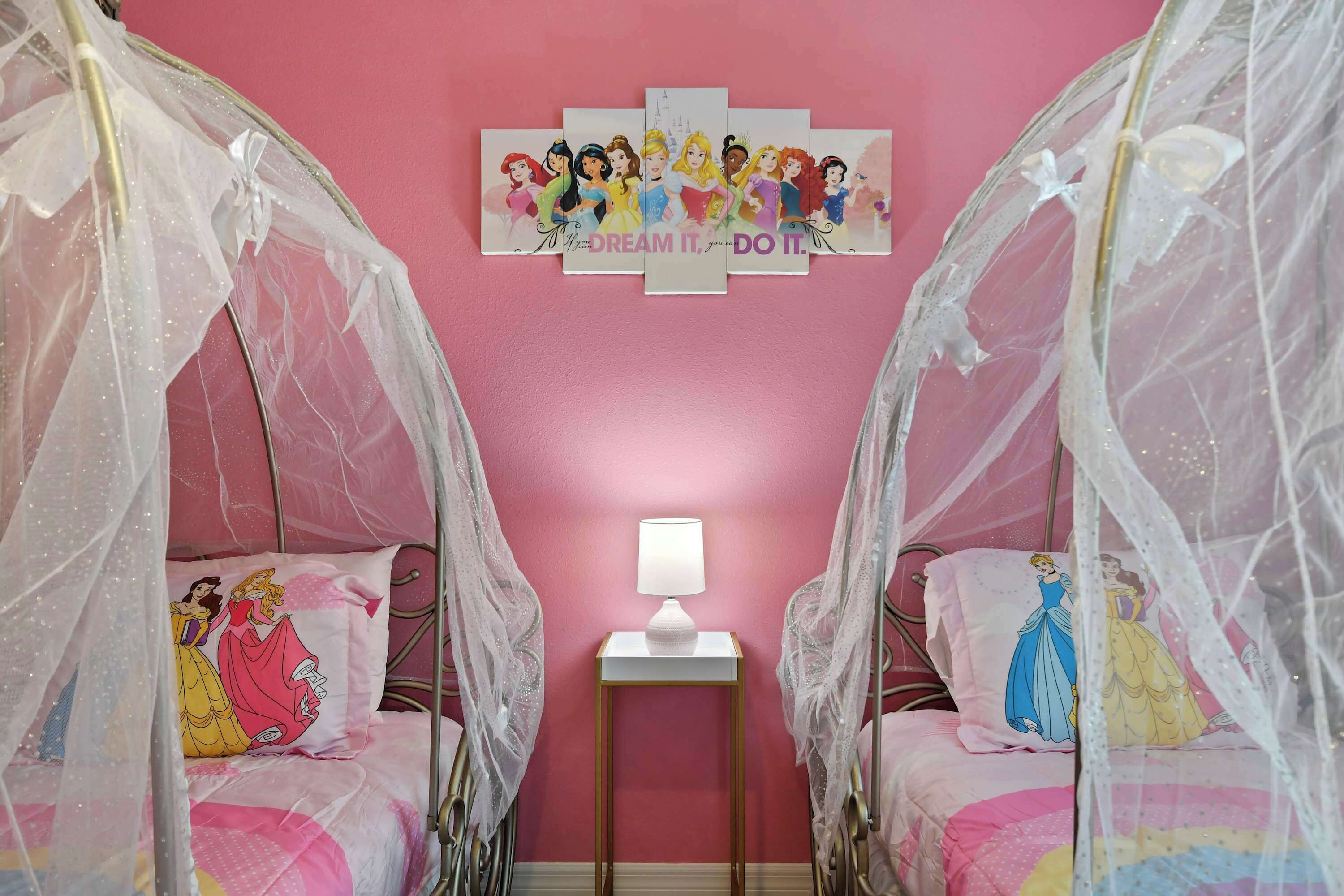 A bedroom with two beds, each with a canopy, a bedside table with a lamp, and a wall decoration.