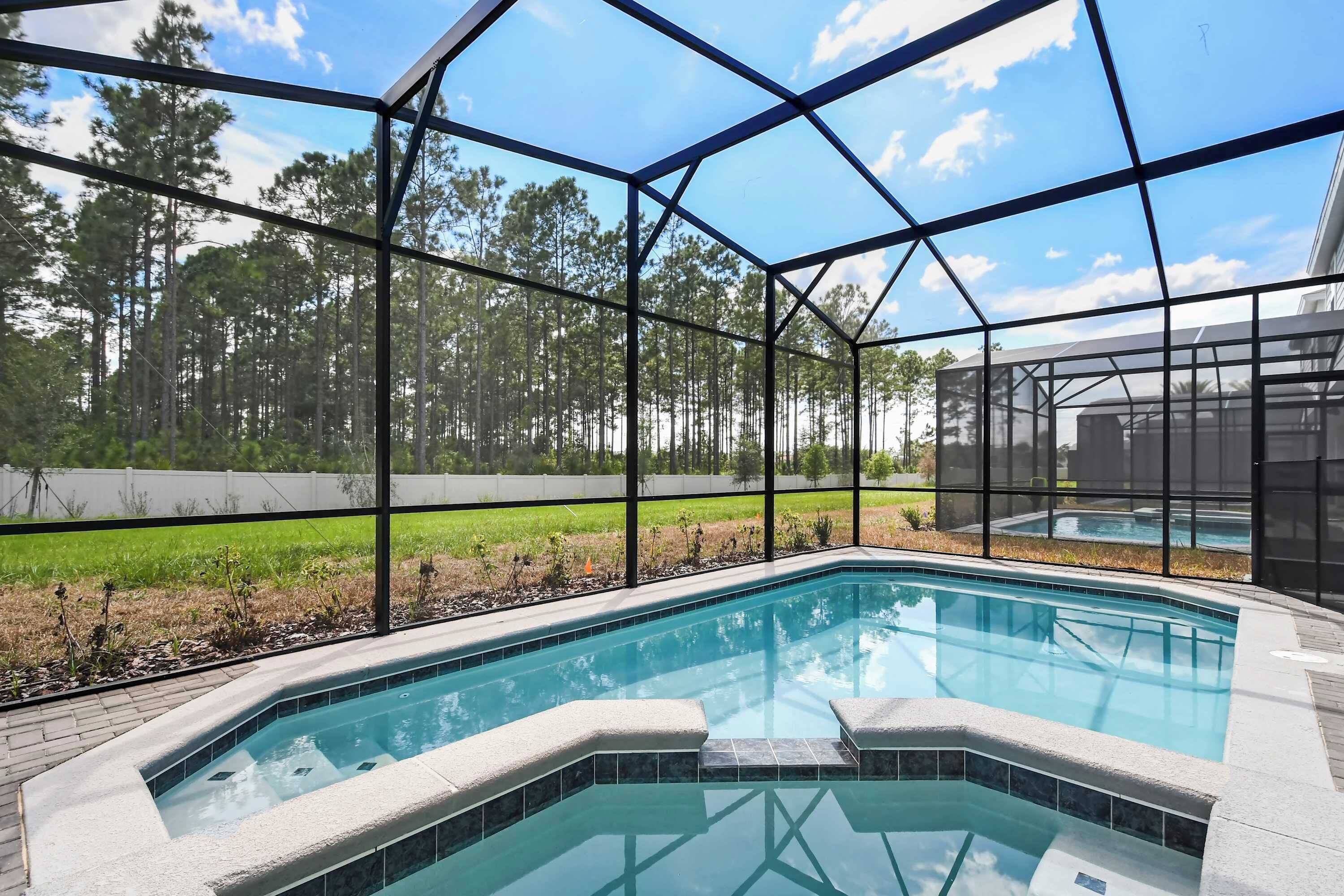 A swimming pool with a glass enclosure, surrounded by a grassy area and trees.