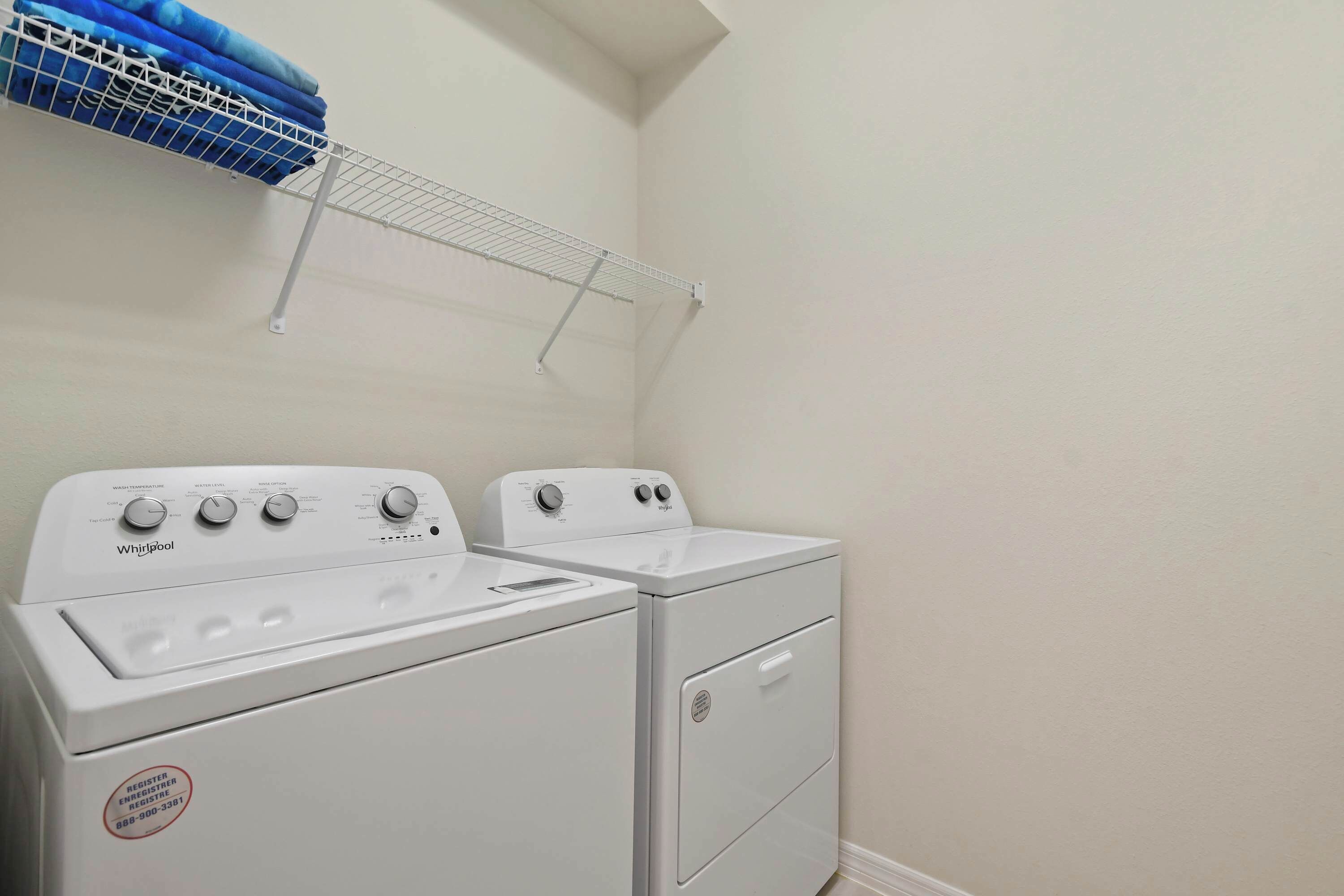 Un espace buanderie comprenant deux lave-linge et deux sèche-linge Whirlpool blancs, un étendoir métallique et un panier à linge bleu.