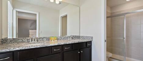 Un baño con tocador de madera oscura, un espejo grande y mampara de ducha de vidrio.