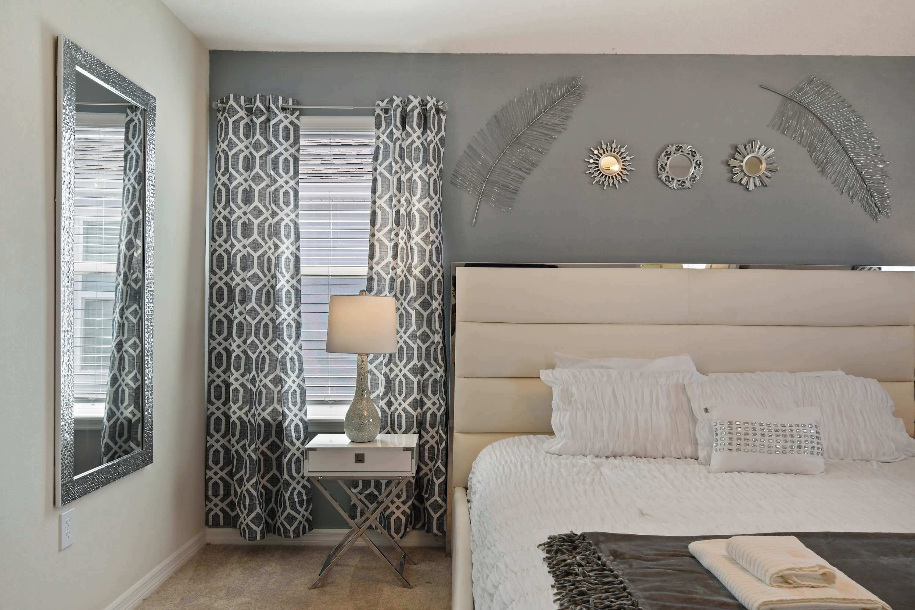 A bedroom with a bed, a nightstand, a lamp, patterned curtains, and wall decorations.