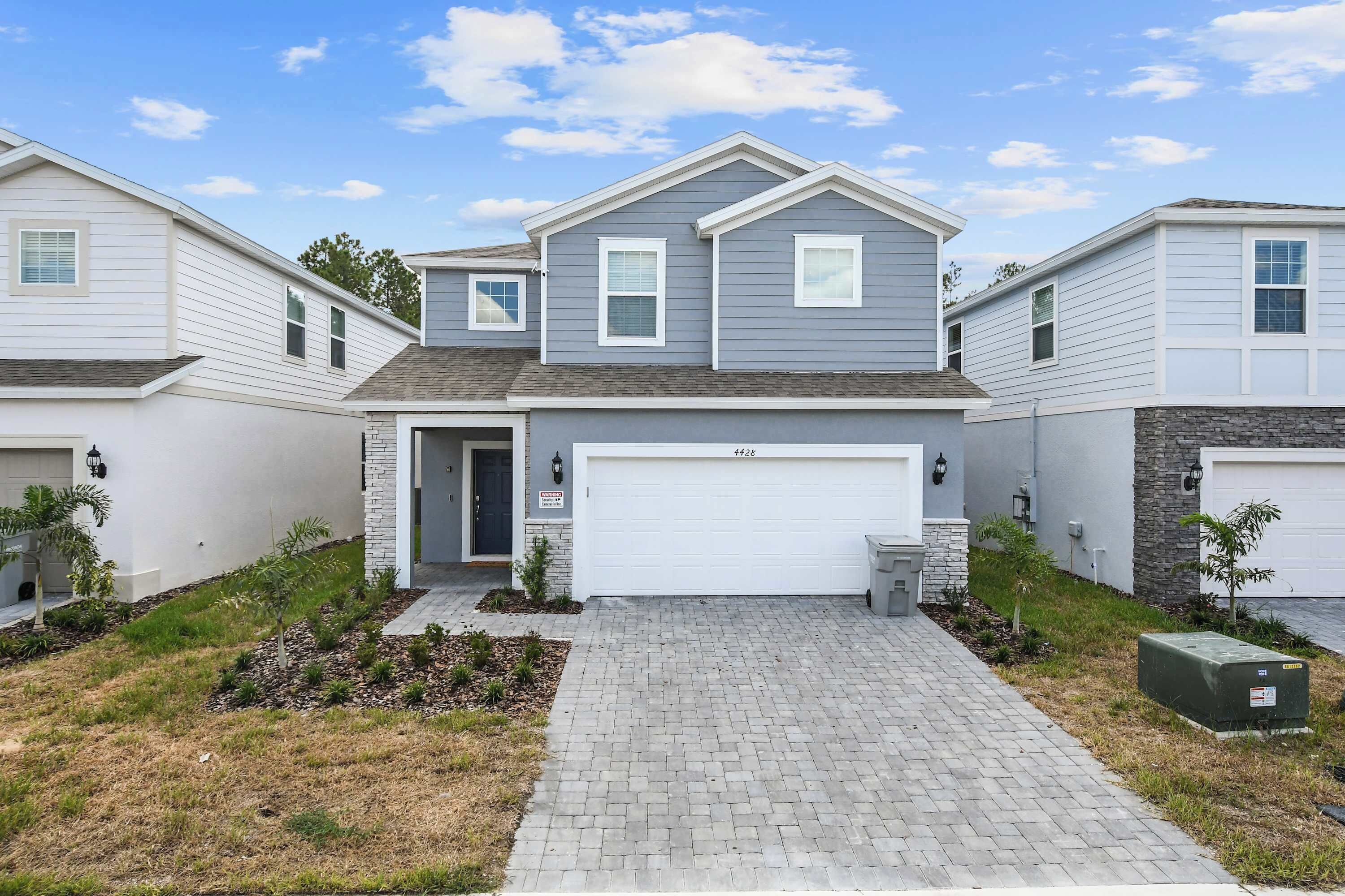 A modern two-story house with a garage, a brick driveway, and small landscaping.