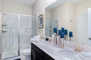 A modern bathroom with two sinks, a glass shower enclosure, and a large mirror.