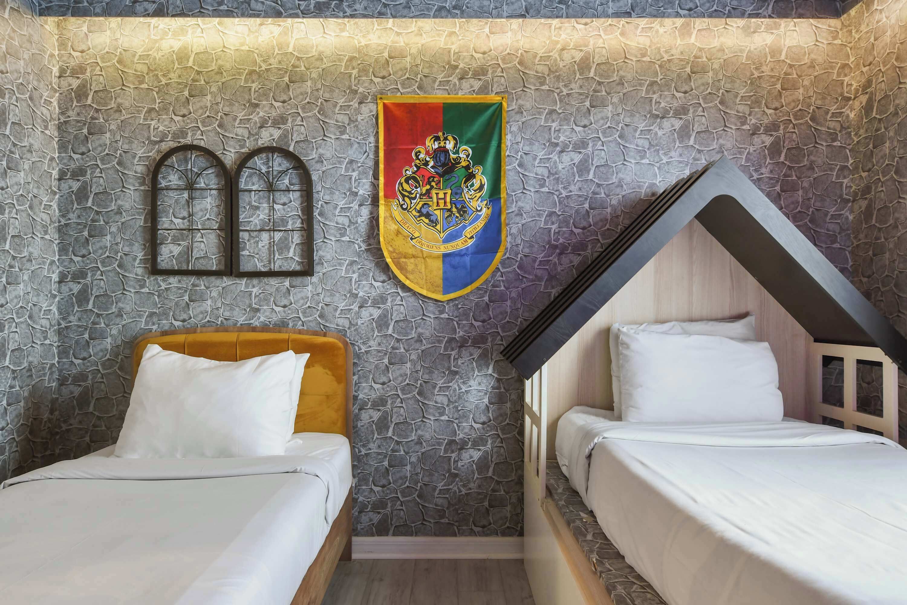 Une chambre avec deux lits, un mur décoré d’un motif en pierre, un drapeau et une fenêtre.