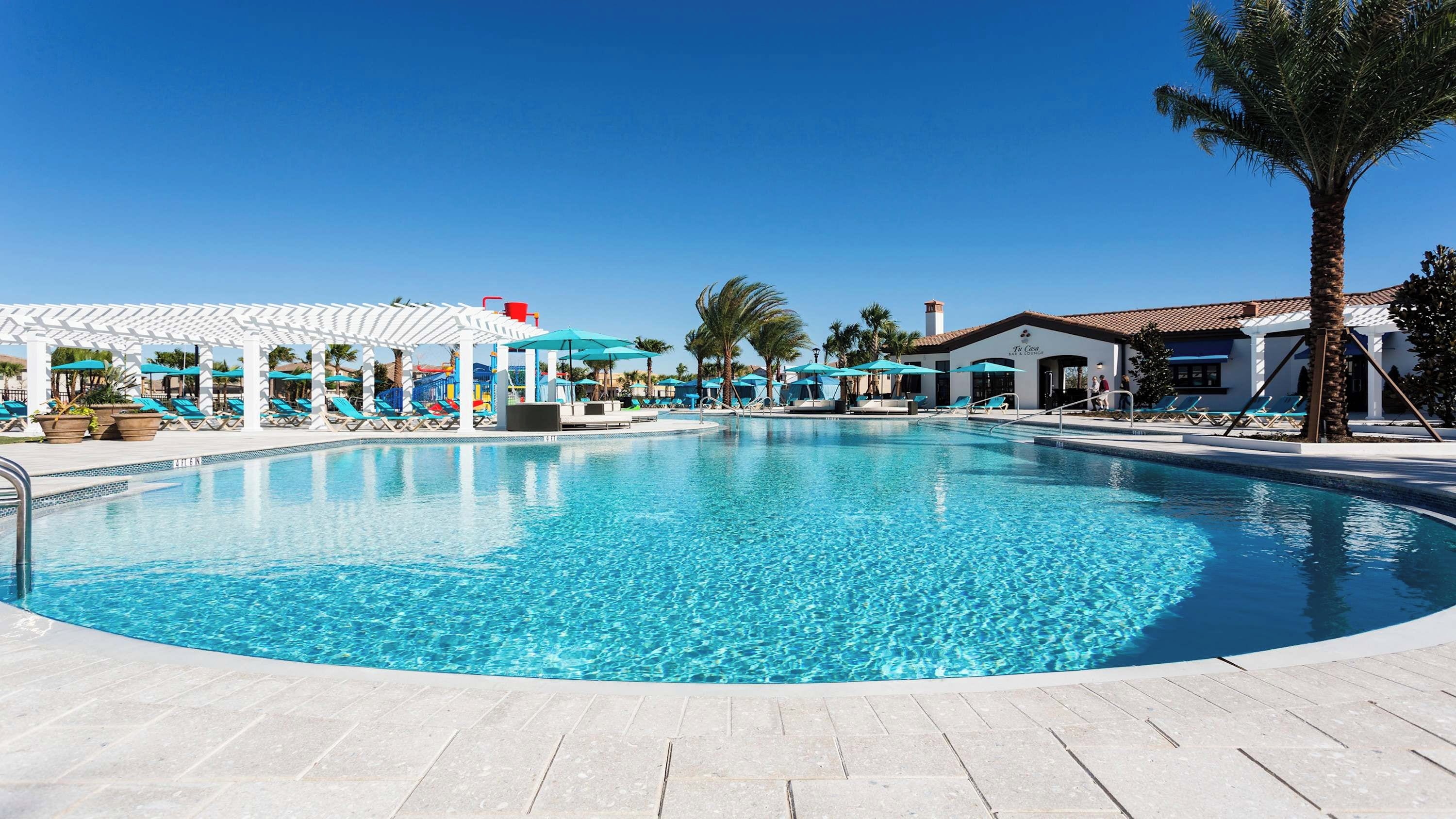 Piscina azul cristalina com espreguiçadeiras e guarda-sóis, rodeada por palmeiras e uma estrutura de pérgula branca.