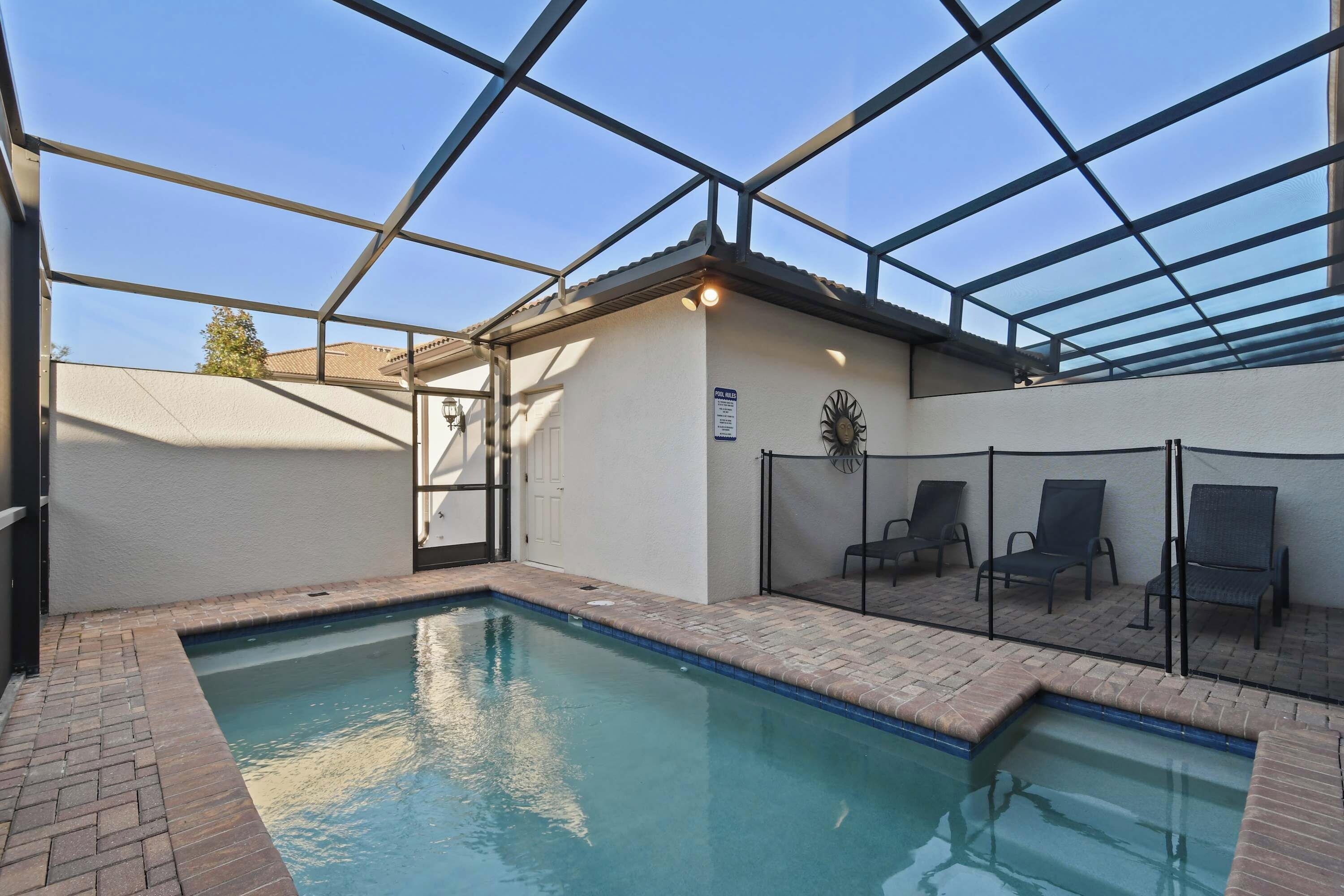 An indoor swimming pool with a clear glass ceiling, a poolside seating area, and a sign indicating pool rules.