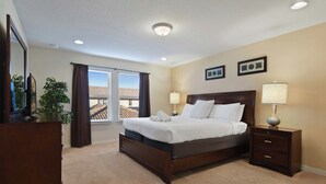 A bedroom with a large bed, two bedside lamps, a nightstand, a dresser, a potted plant, and a window with blinds. - Free Waterpark Access! 5br Resort Townhome w/ Pool (Kissimmee)