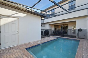 A swimming pool with a glass ceiling, a door, and a patio area with outdoor furniture.