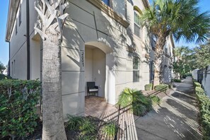 A building with a covered outdoor seating area, a palm tree, and a paved walkway.