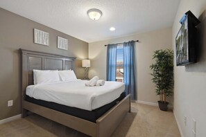 A hotel room with a bed, a flat-screen TV, a potted plant, and a window with curtains. - Free Waterpark Access! 5br Resort Townhome w/ Pool (Kissimmee)