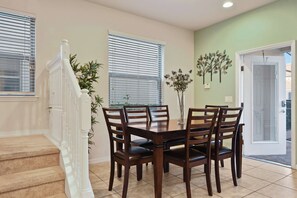 A dining area with a table and chairs, a staircase, and a door leading outside.