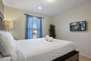 A hotel room with a bed, a lamp, a window with curtains, a plant, and a painting on the wall.