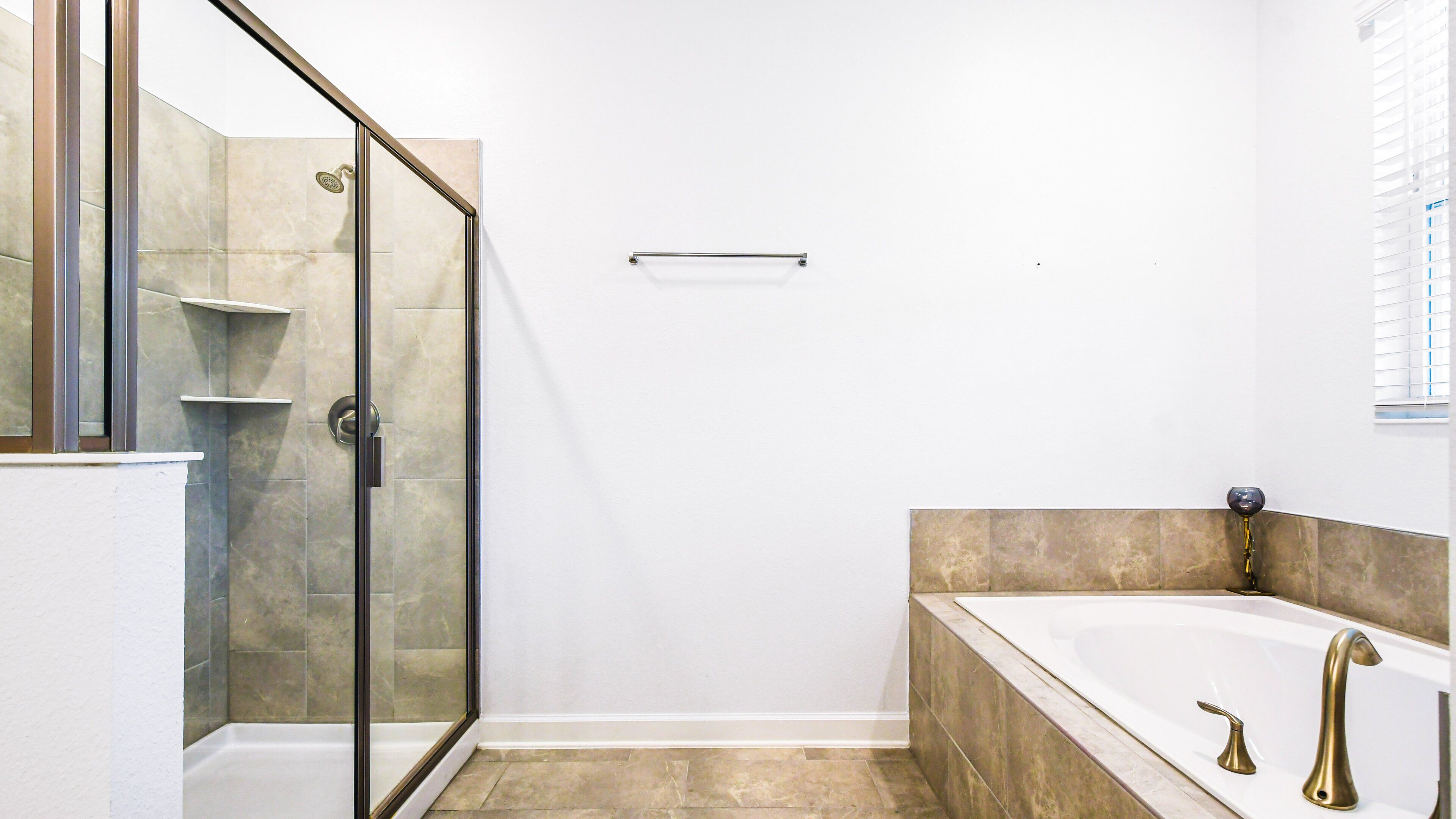 A modern bathroom with a glass-enclosed shower, a bathtub with a gold faucet, and a white vanity.