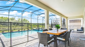 A covered outdoor area with a pool, seating, and a view of the landscape.