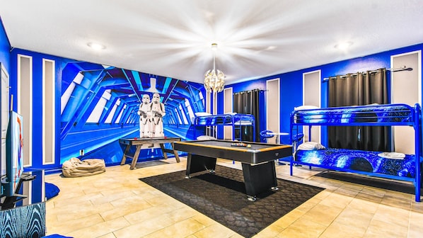 A room with a pool table, bunk beds, and a Star Wars-themed wall.