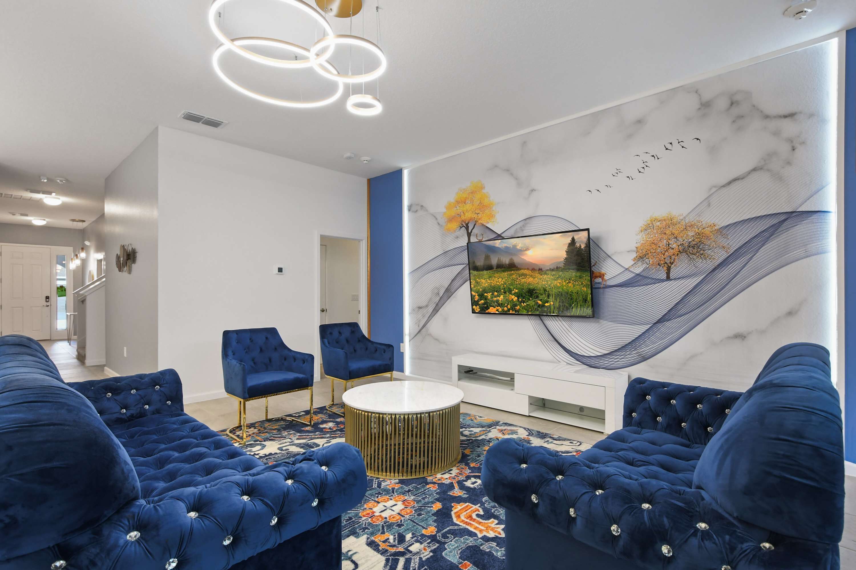 Een moderne woonkamer met een grote televisie, blauwe banken en een kamerkleed met een patroon.