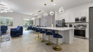 A modern kitchen with white cabinets, stainless steel appliances, and a central island with bar stools. - Family-friendly Luxury Home Near Disney & More (Kissimmee)