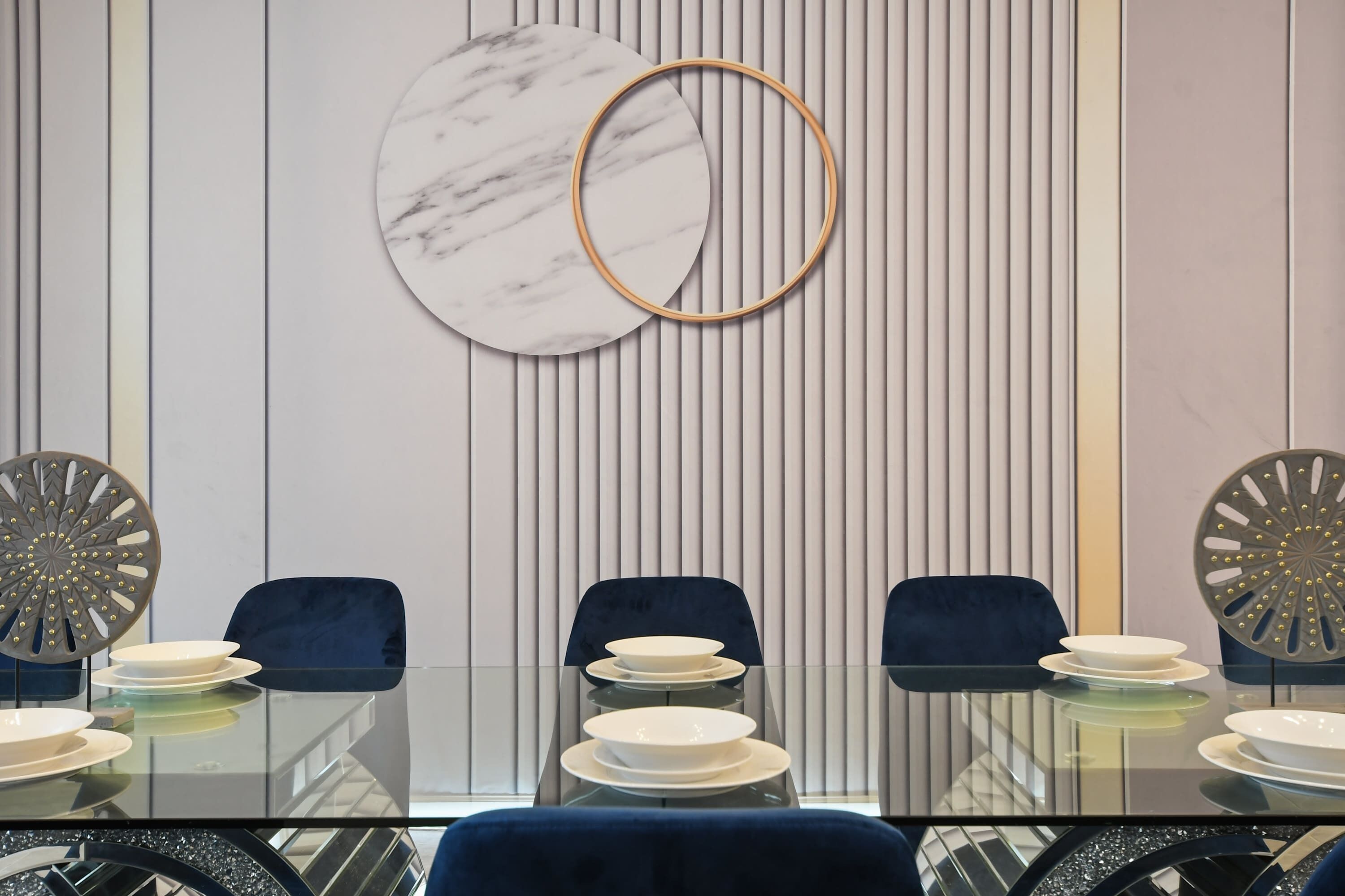 A conference room with a glass table, blue chairs, and a marble wall decoration.